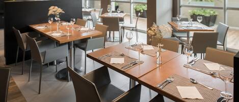 A modern restaurant with multiple tables, each set with cutlery, napkins, and wine glasses.
