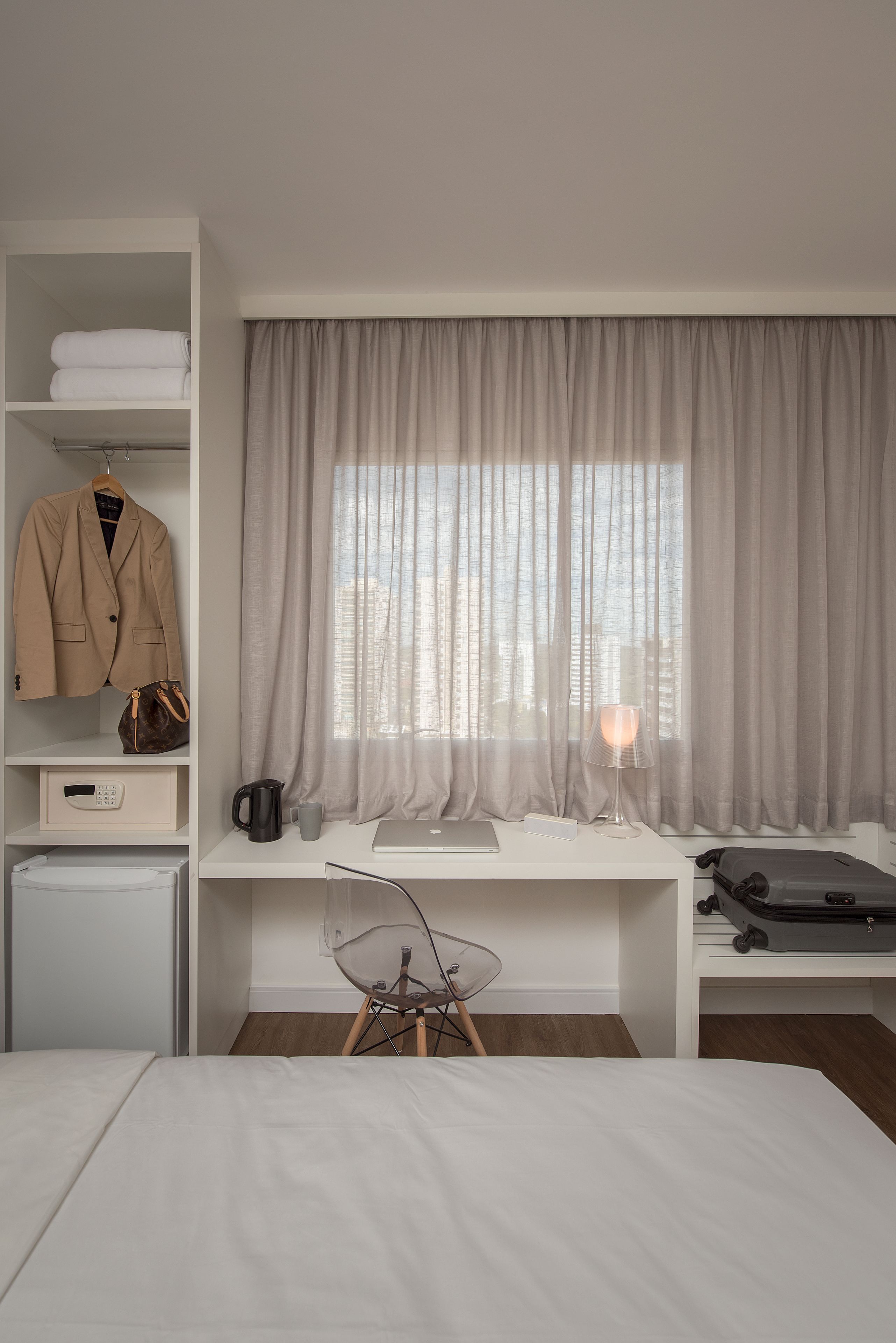 Habitación de hotel con cama, escritorio con ordenador portátil, silla, armario y ventana con cortinas.