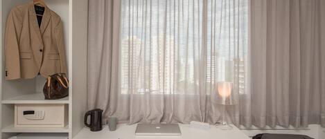Habitación de hotel con cama, escritorio con ordenador portátil, silla, armario y ventana con cortinas.