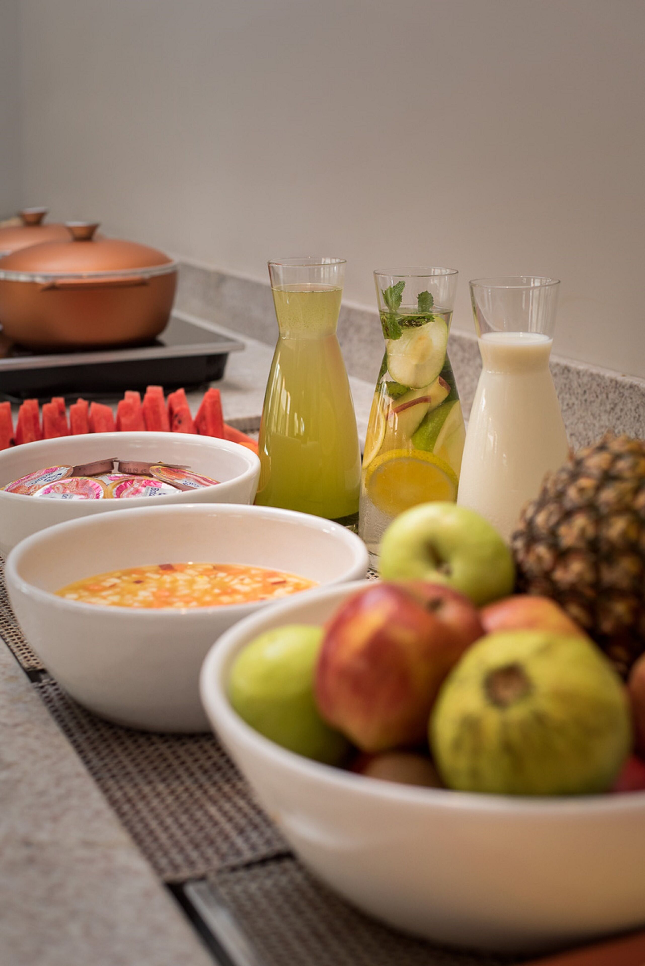 Une table sur laquelle on trouve divers aliments, notamment des fruits, un bol de yaourt, un verre de jus et une bouteille de lait.