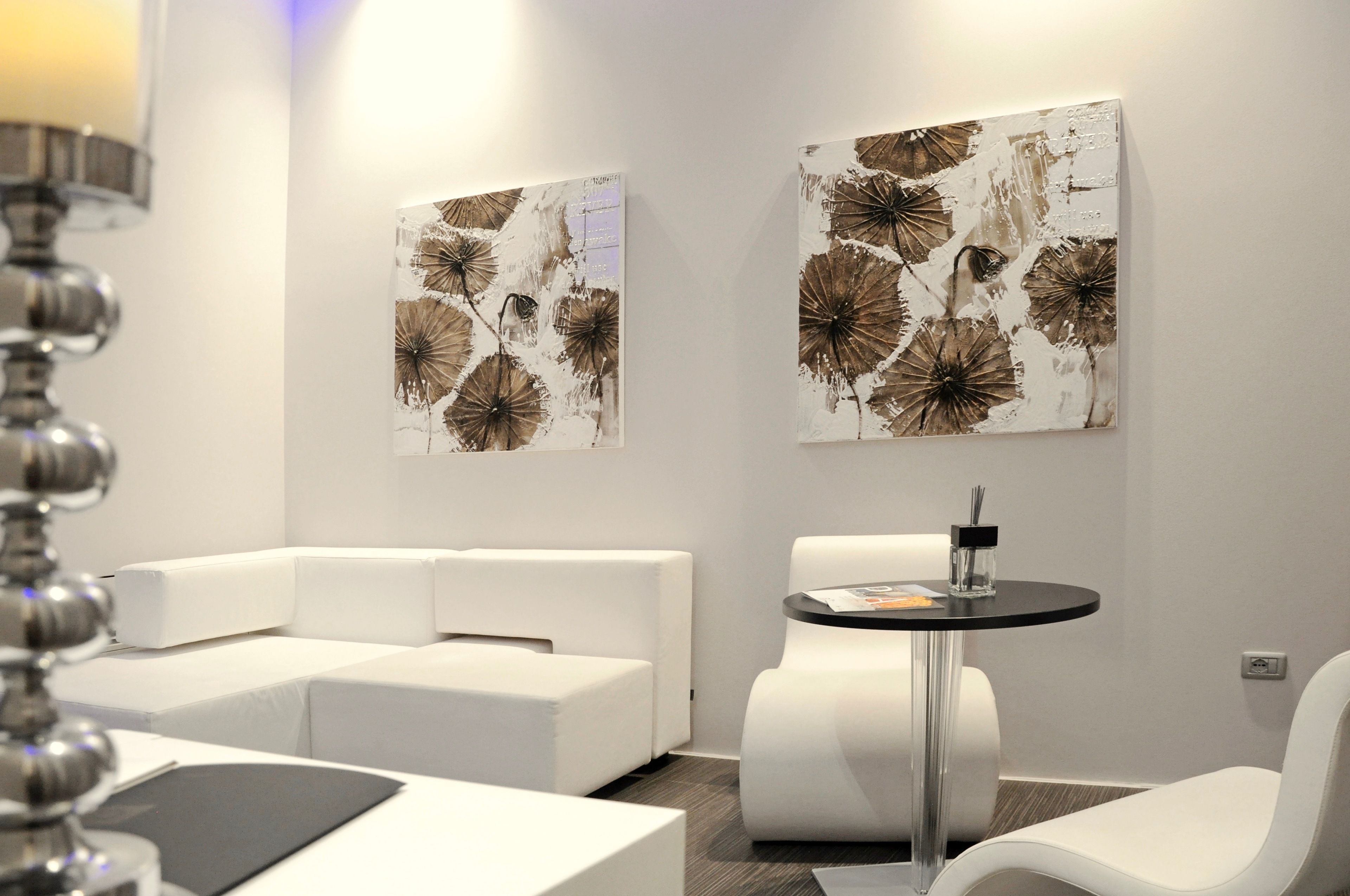 Habitació d'hotel moderna amb un sofà modular blanc, una taula rodona amb tapa negra i dos quadres abstractes grans a la paret.