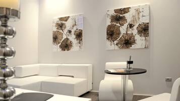 Habitació d'hotel moderna amb un sofà modular blanc, una taula rodona amb tapa negra i dos quadres abstractes grans a la paret.