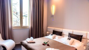 A hotel room with a bed, a bedside table, a chair, and a window with curtains. - Le Camp Suite & SPA (Padova)