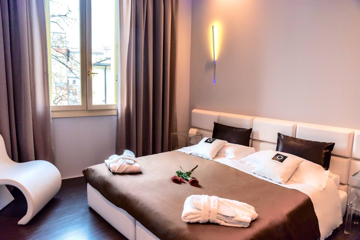 A hotel room with a bed, a bedside table, a chair, and a window with curtains.