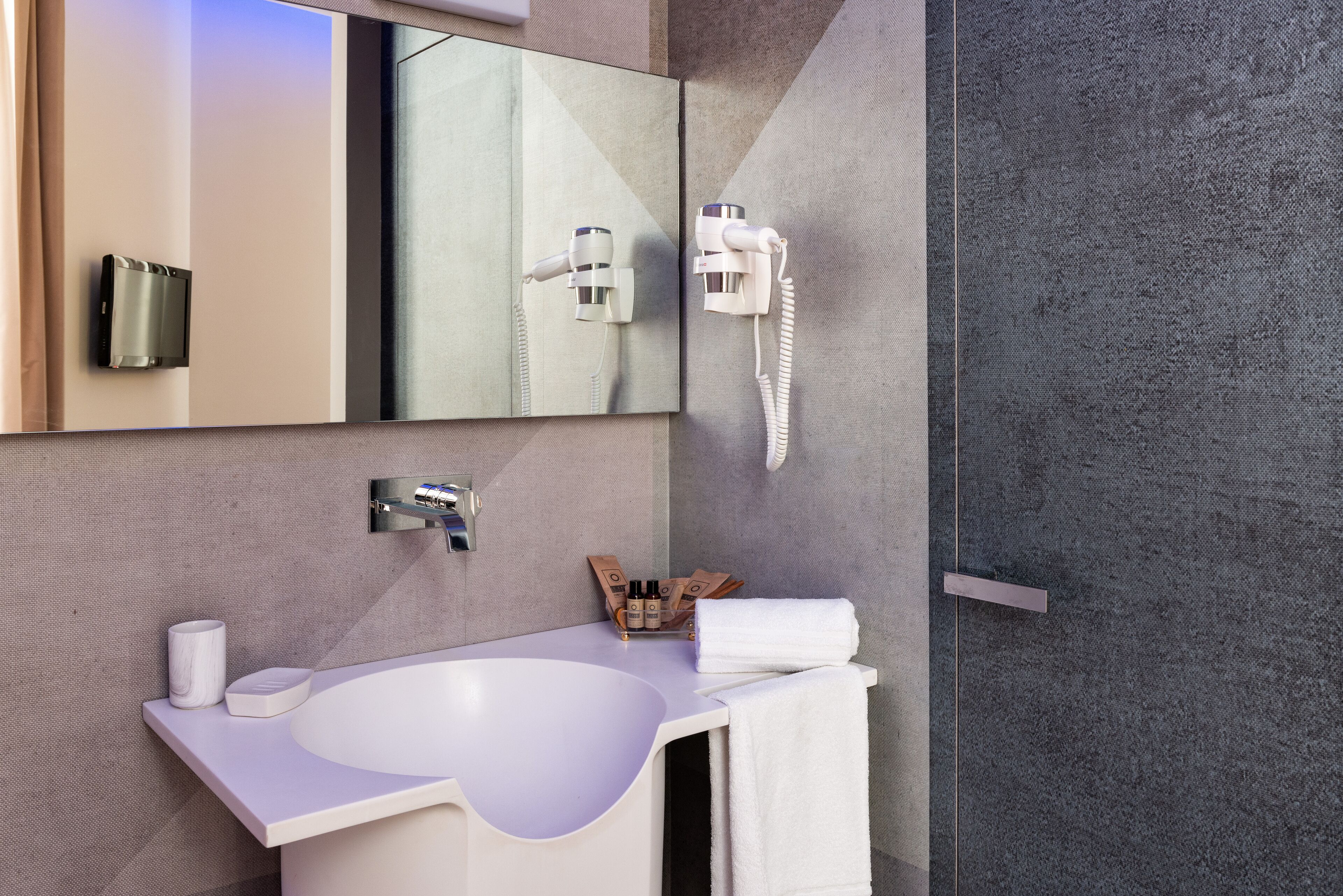 A modern bathroom with a white sink, a mirror, a hairdryer, and a towel rack.