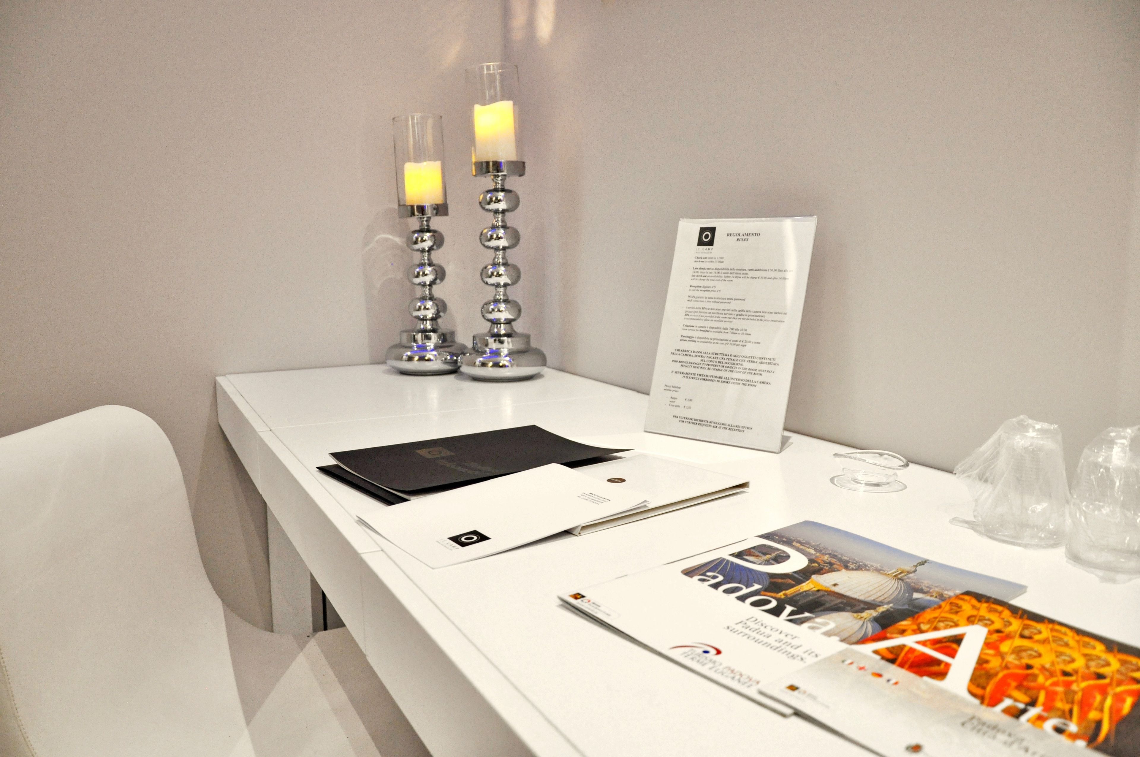 A white reception desk with a black folder, a white envelope, a pen, a brochure, and two lit candles on a stand.