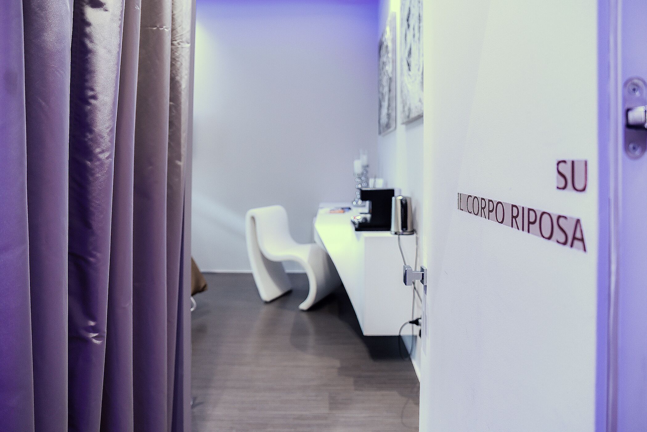 A reception area with a white desk, a white chair, and a sign that reads "SU IL CORPO RIPOSA".