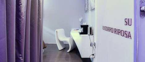 A reception area with a white desk, a white chair, and a sign that reads "SU IL CORPO RIPOSA".