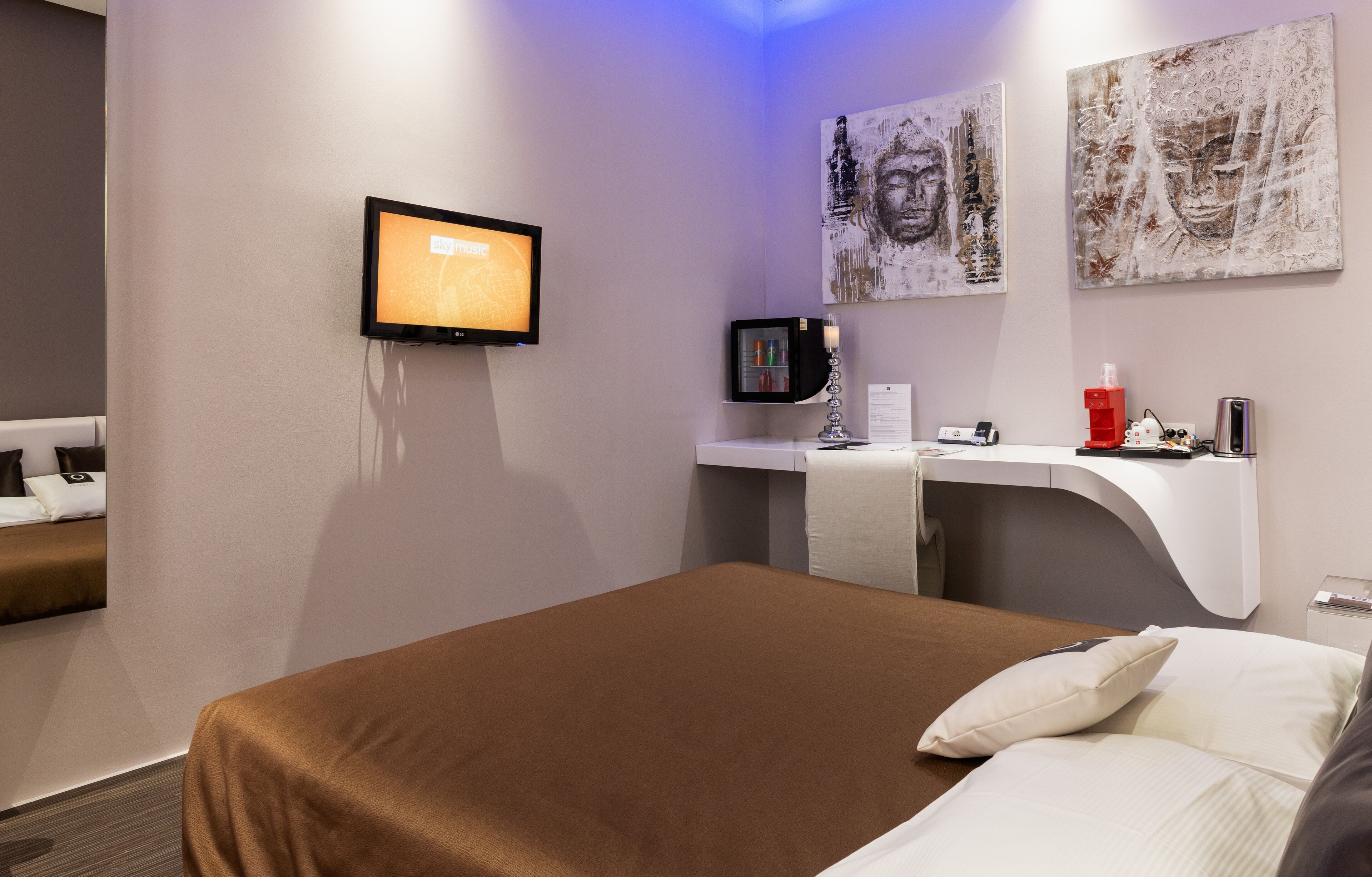 Ein modernes Hotelzimmer mit einem großen Bett, einem Flachbildfernseher, einem kleinen Schreibtisch mit Computer und Bildern an den Wänden.