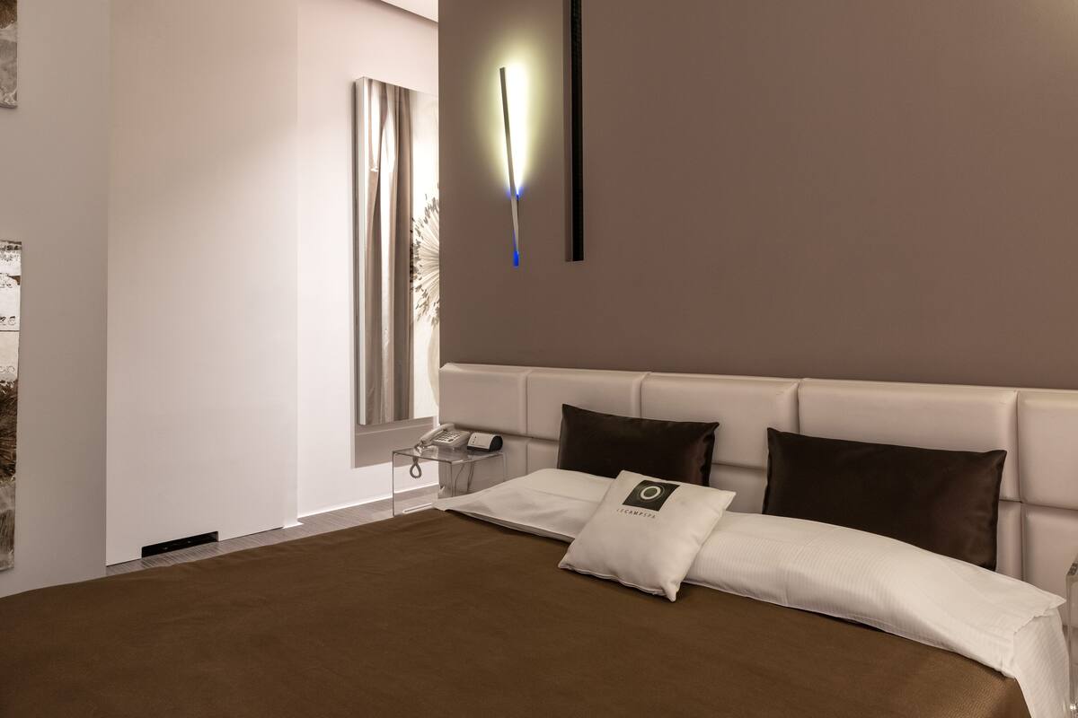A modern hotel room with a large bed, a bedside table with a phone, and a wall-mounted light fixture.