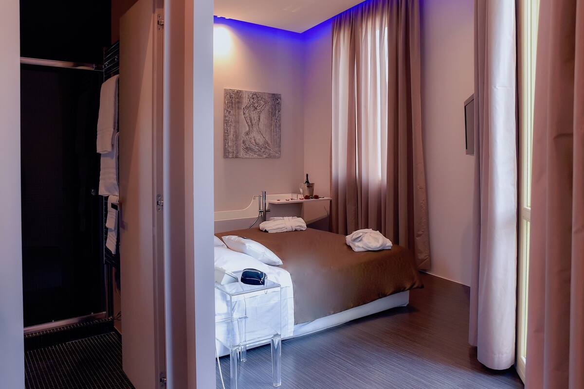A hotel room with a bed, a bedside table, a mirror, and a painting on the wall.