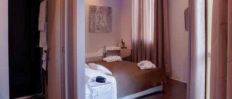 A hotel room with a bed, a bedside table, a mirror, and a painting on the wall.