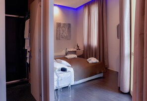 A hotel room with a bed, a bedside table, a mirror, and a painting on the wall.
