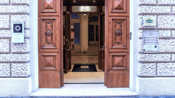 A hotel entrance with wooden double doors, a reception area, and a sign indicating a suite and spa. - Le Camp Suite & SPA (Padova)