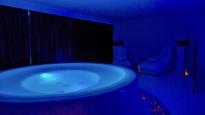 A modern bathroom with a large, illuminated bathtub, a dark wooden panel wall, and a white sink area. - Le Camp Suite & SPA (Padova)