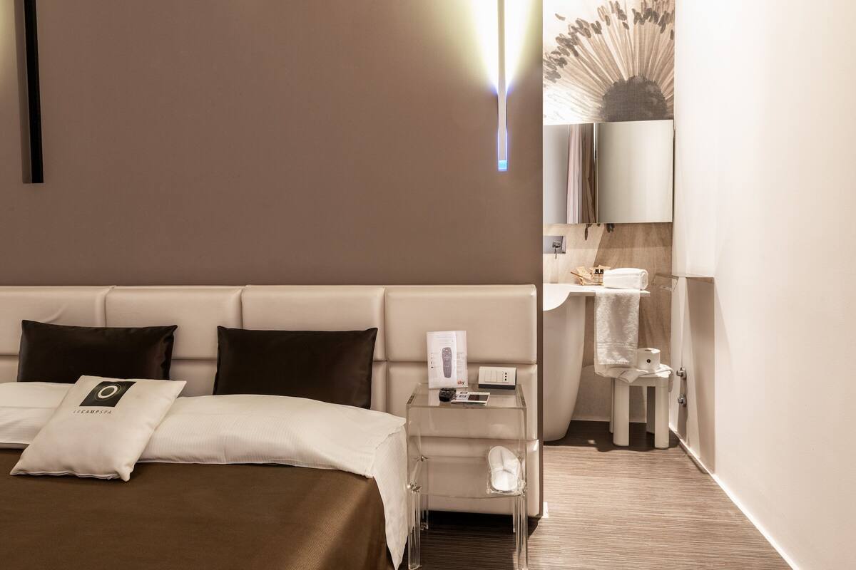 A hotel room with a bed, a nightstand, a bathroom, and a mirror.
