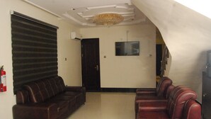 A lobby with a dark brown leather sofa, a red leather sofa, a chandelier, a flat-screen TV, and a closed door.