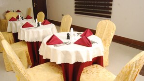 A dining area with round tables covered in white tablecloths, red napkins, and gold chairs.