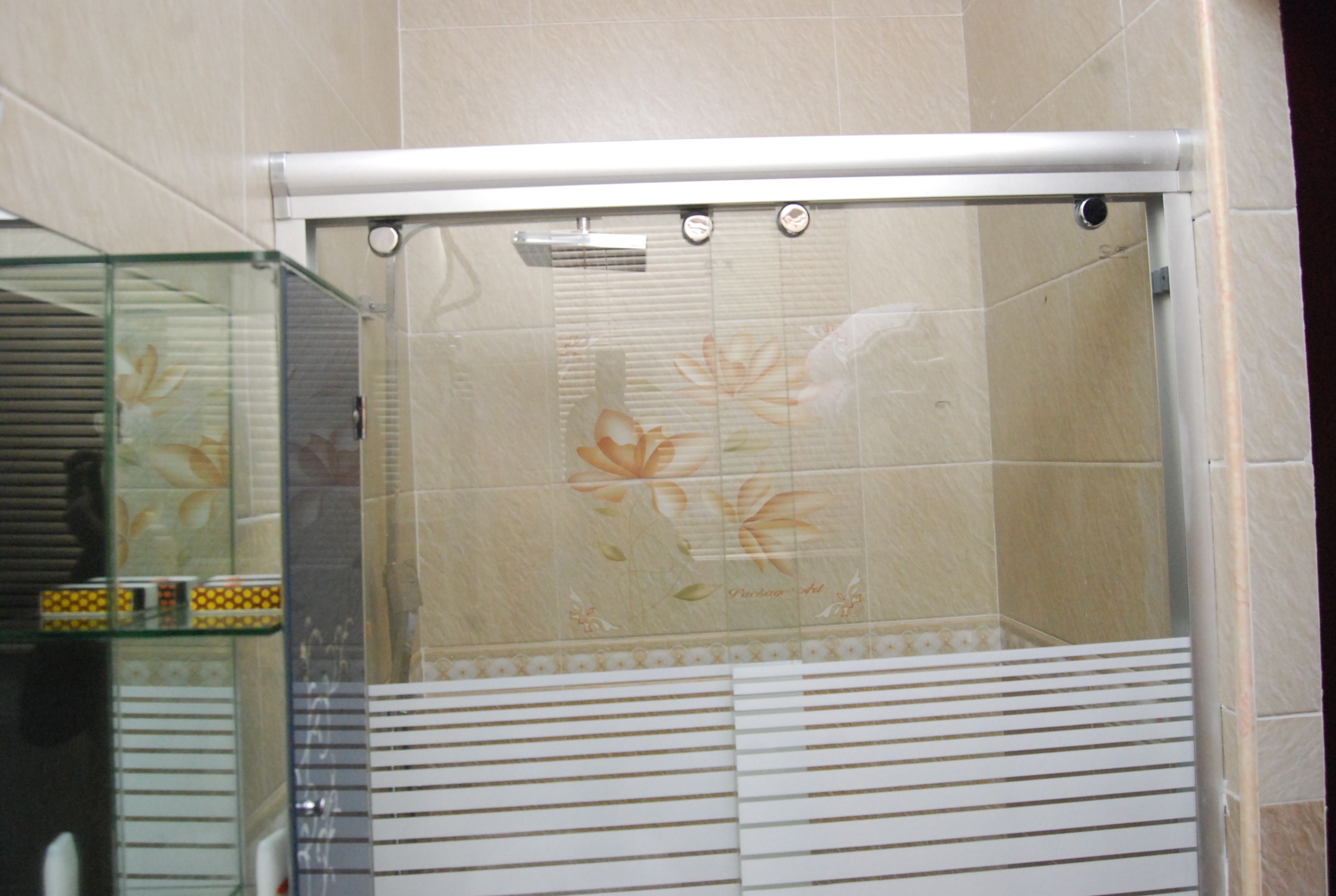 Ducha con puerta de cristal, azulejos color beige y un diseño floral.