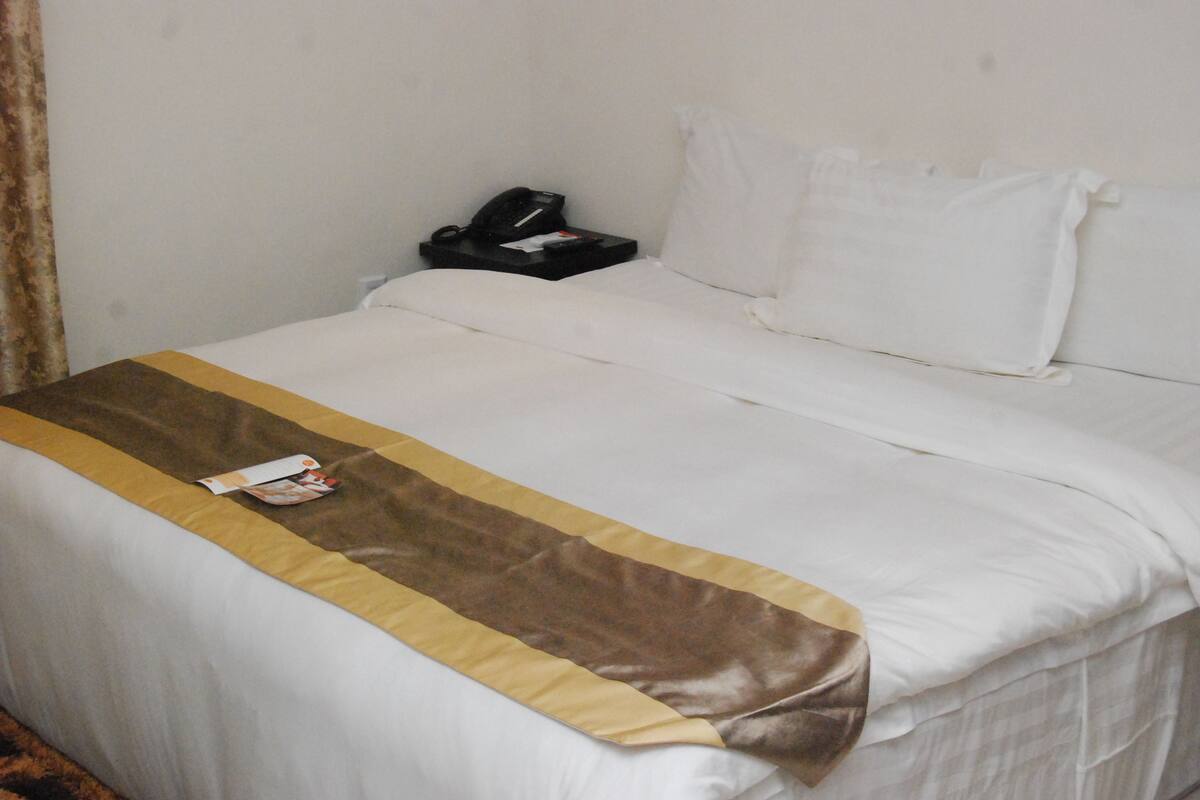 A hotel room with a neatly made bed, a bedside telephone, and a brown and beige decorative strip.