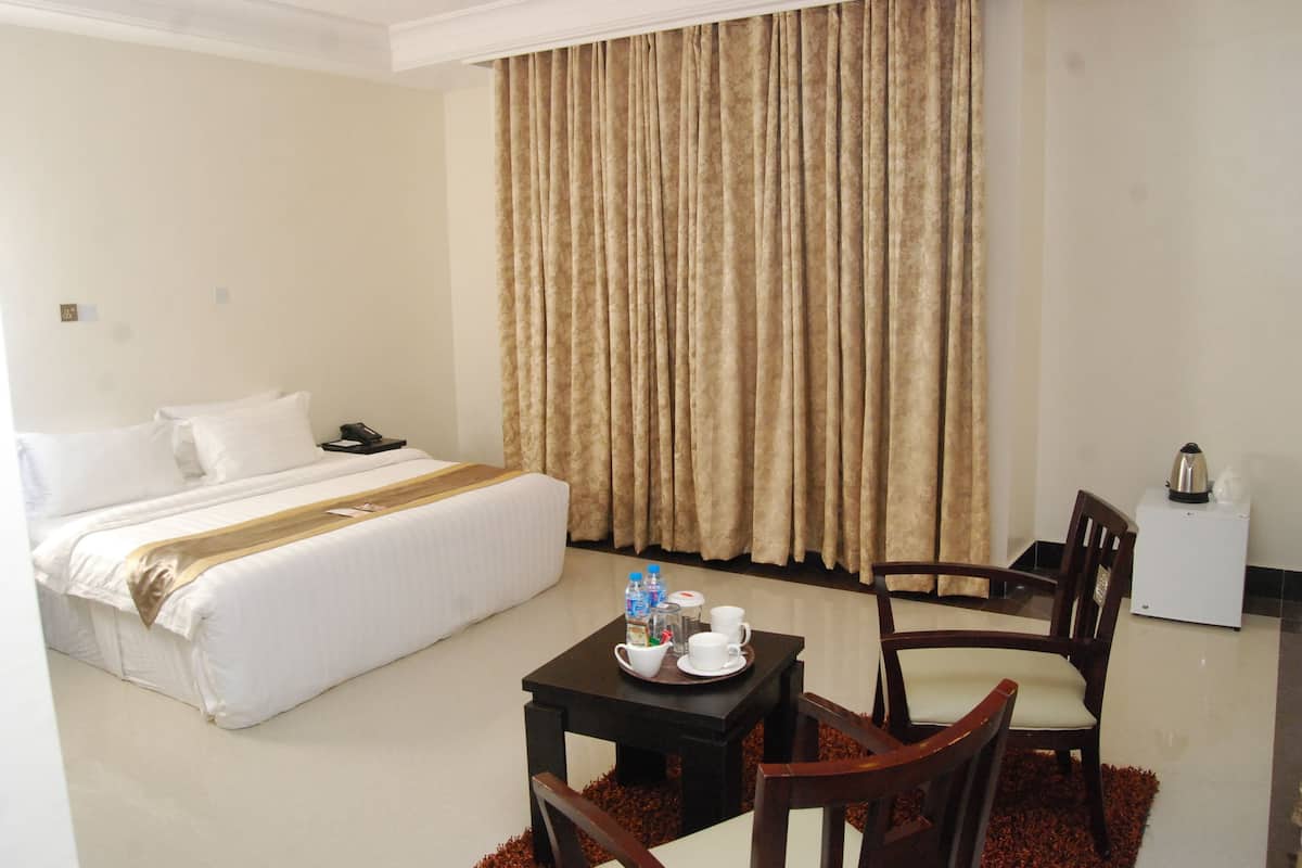 A hotel room with a bed, a small table with a tray of breakfast items, a chair, and a desk with a kettle.