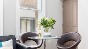 A modern room with a glass table, two leather chairs, a vase with flowers, and a bottle of wine. - One Bed Serviced Apts near Oxford Street (London)
