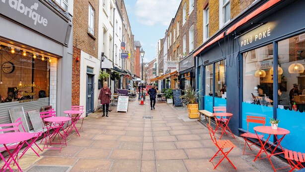 A narrow street with outdoor seating, shops on either side, and a clear sky. - One Bed Serviced Apts near Oxford Street (London)