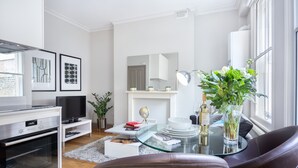 A modern living room with a glass coffee table, leather chairs, a flat-screen TV, a white fireplace, and a large window with a view. - One Bed Serviced Apts near Oxford Street (London)