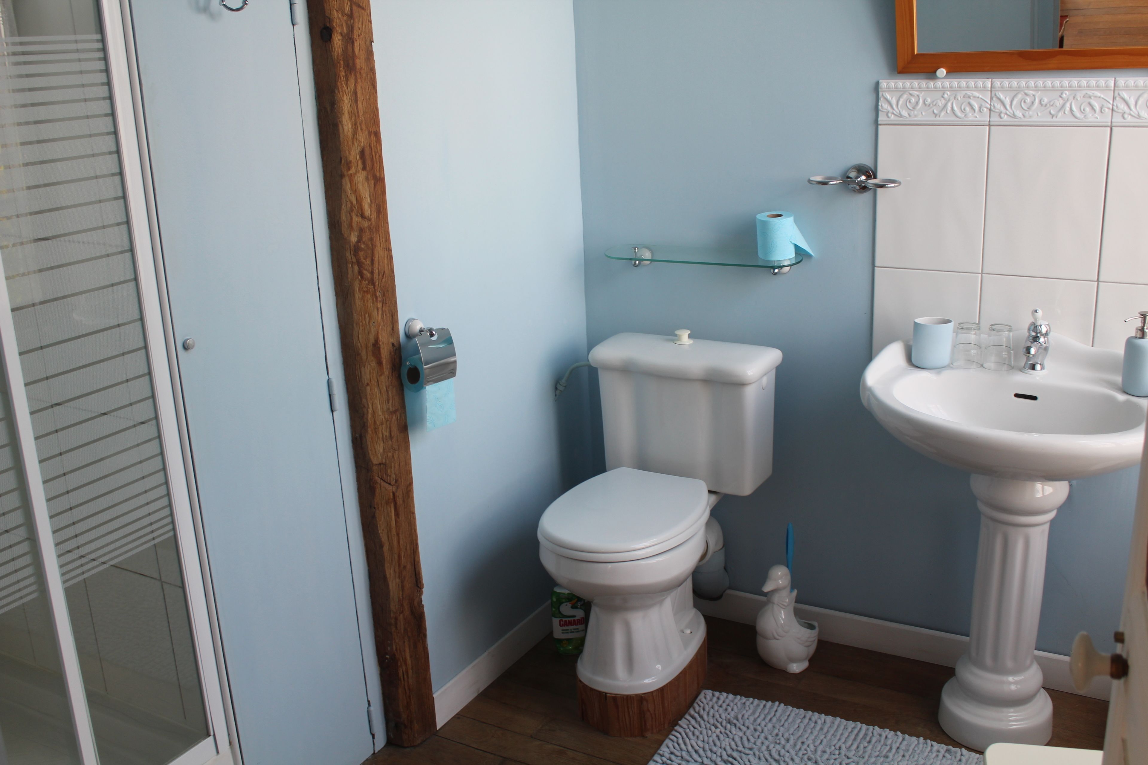 A bathroom with a toilet, sink, and a glass shelf with a roll of toilet paper.