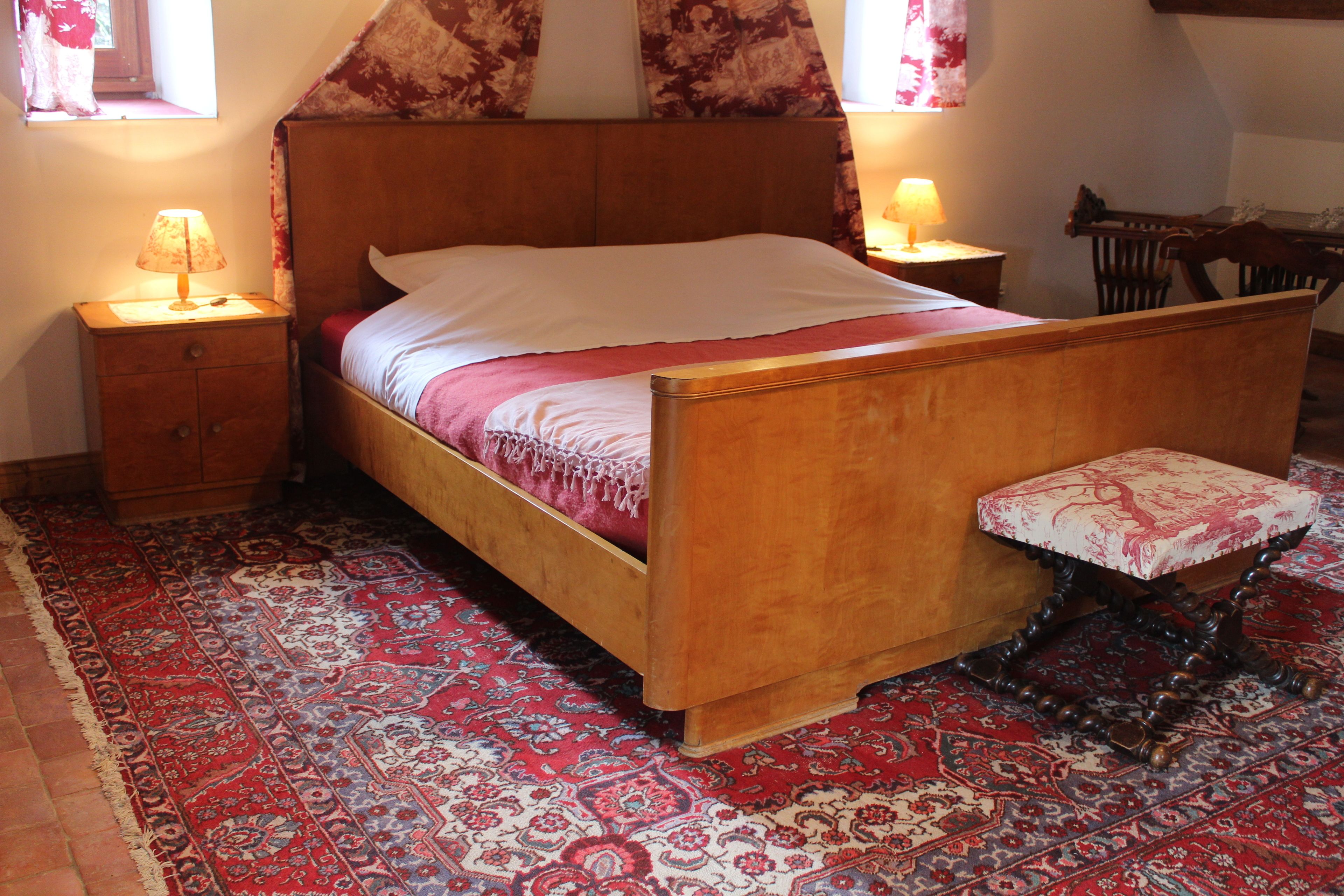 A wooden bed with a matching bench, a patterned rug, and two bedside lamps.