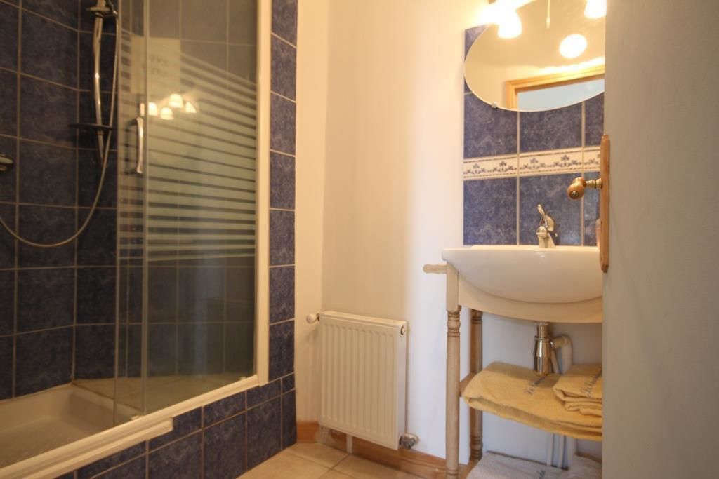 Un baño con ducha de vidrio, un lavamanos blanco y pared con azulejos.