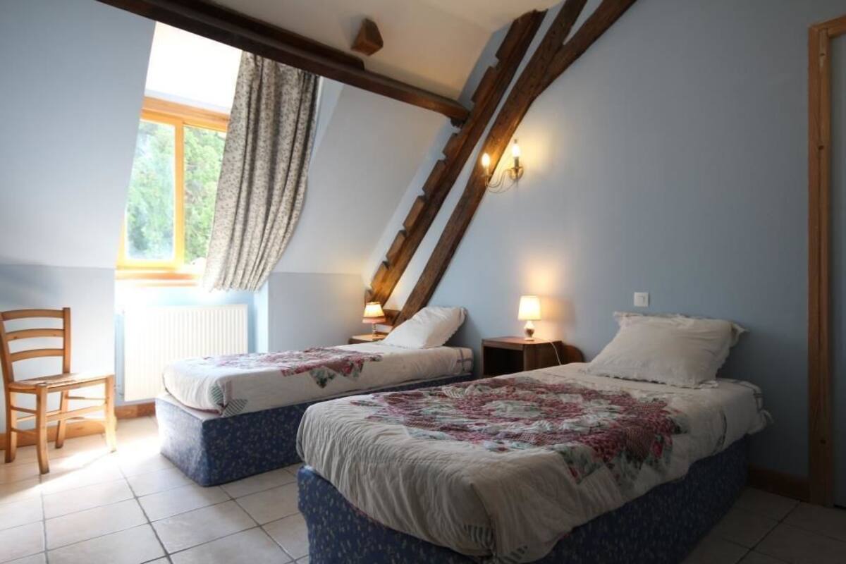 A bedroom with two beds, a wooden chair, and a window with curtains.