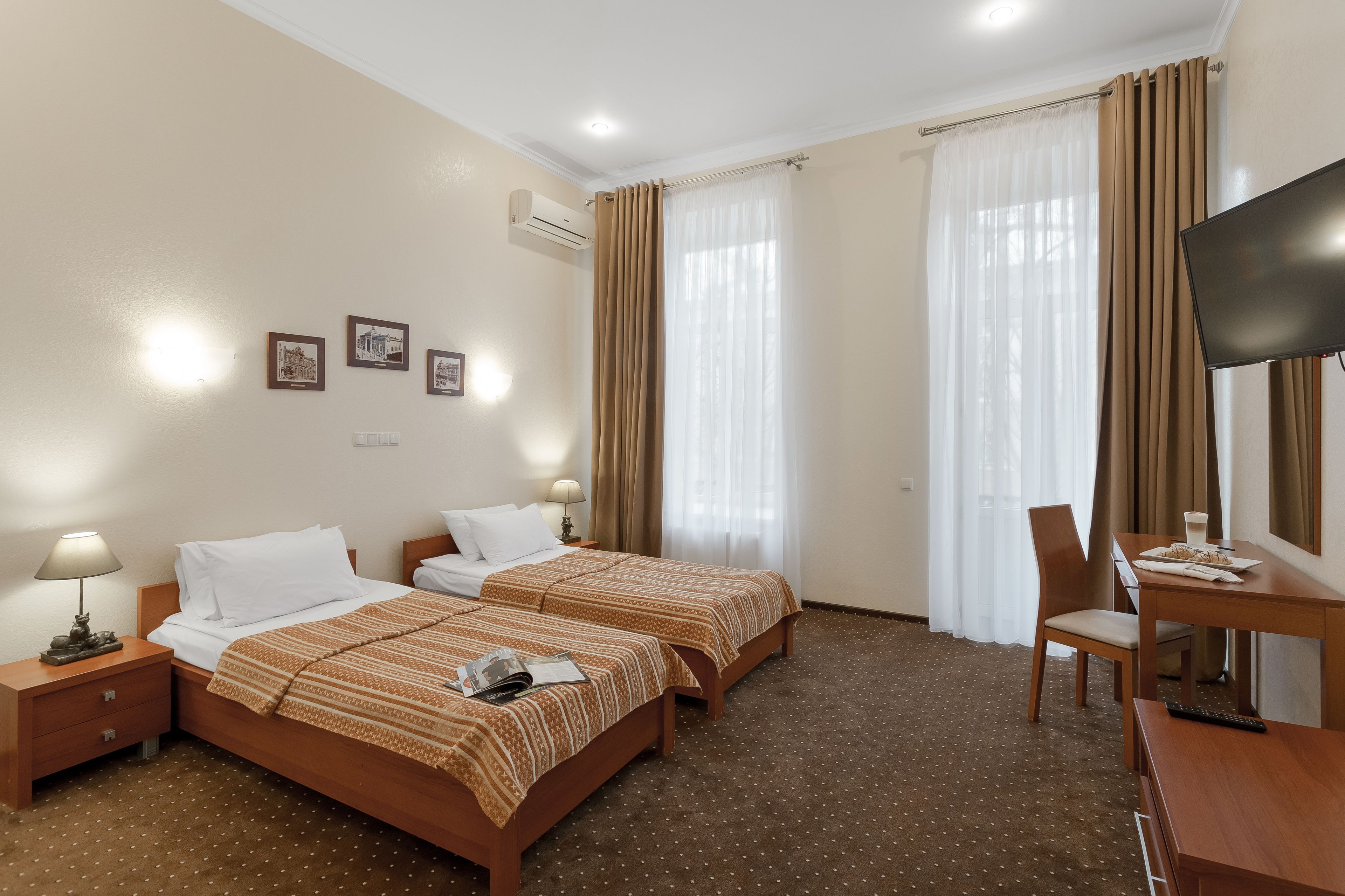 A hotel room with two beds, a desk, a chair, a television, and a window with curtains.