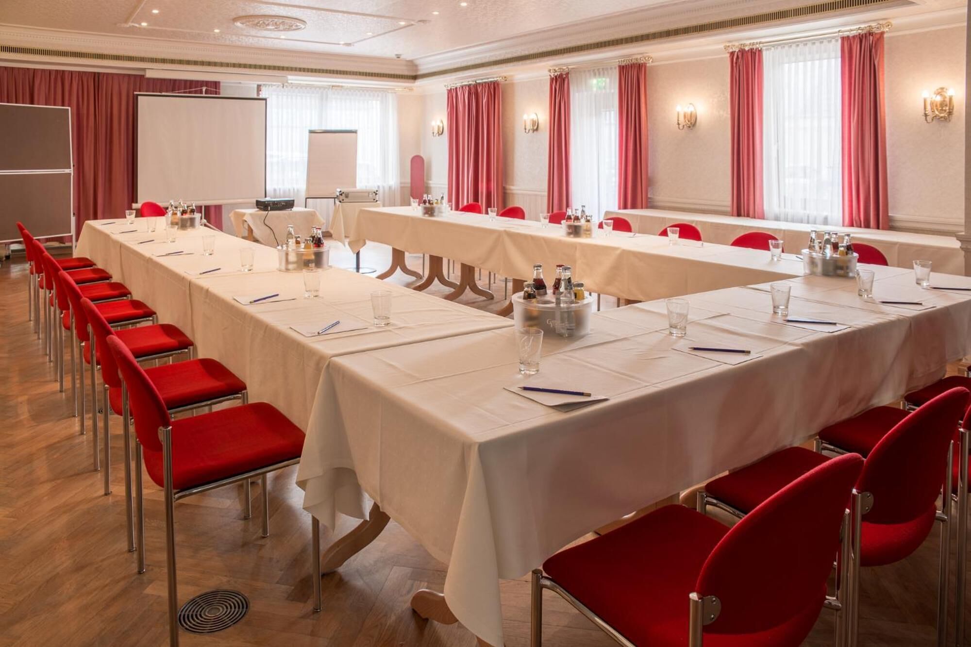 A conference room with long tables, red chairs, and a whiteboard.