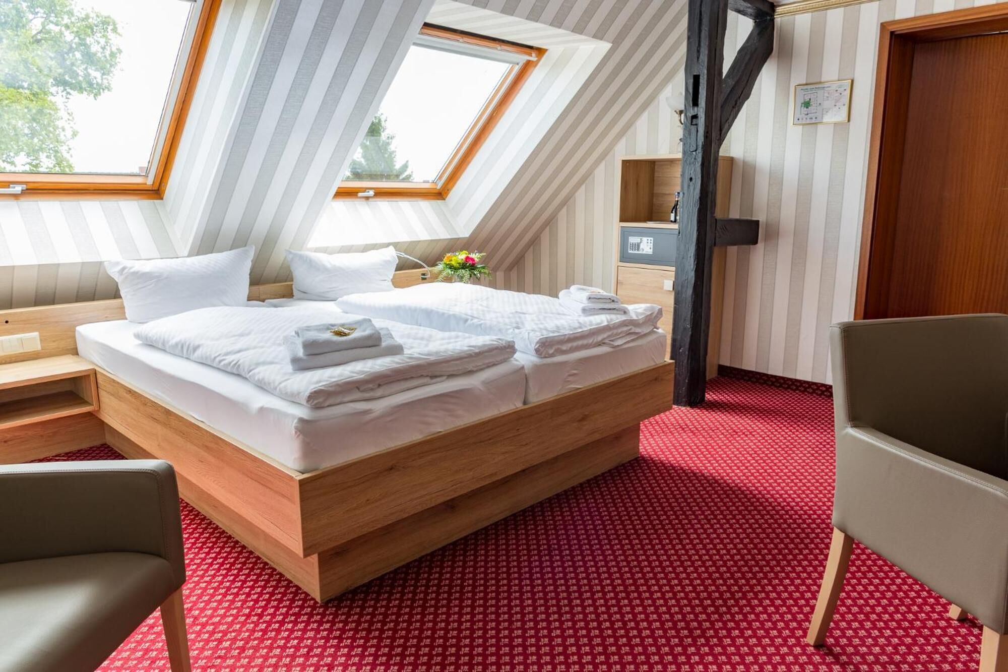 Un dormitorio moderno con techo inclinado, estructura de cama de madera, alfombra roja estampada y un pequeño escritorio con silla.