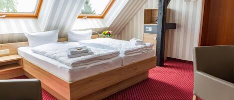 Un dormitorio moderno con techo inclinado, estructura de cama de madera, alfombra roja estampada y un pequeño escritorio con silla.