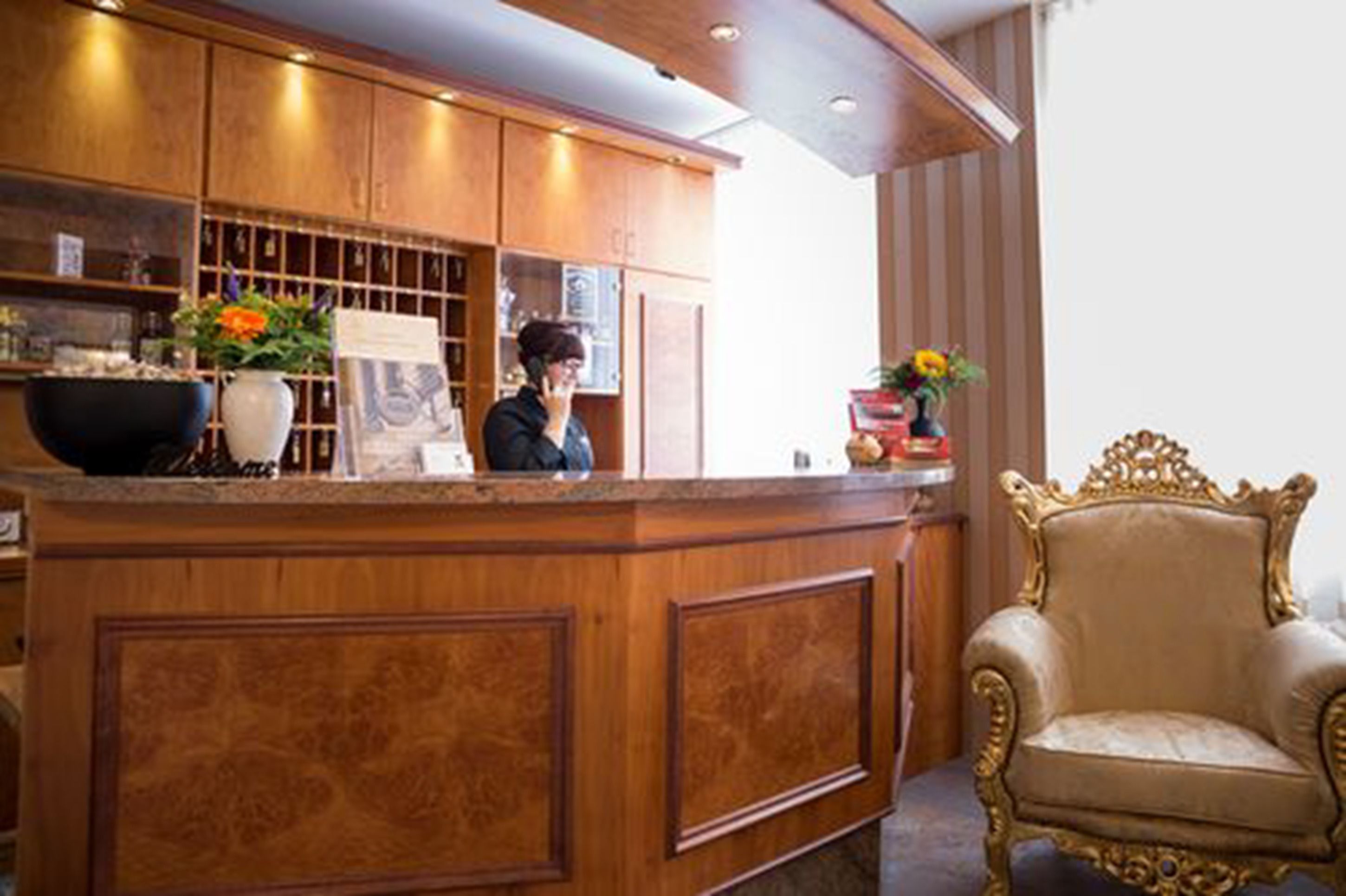 Un área de recepción con mostrador de madera, una silla dorada y jarrones decorativos.