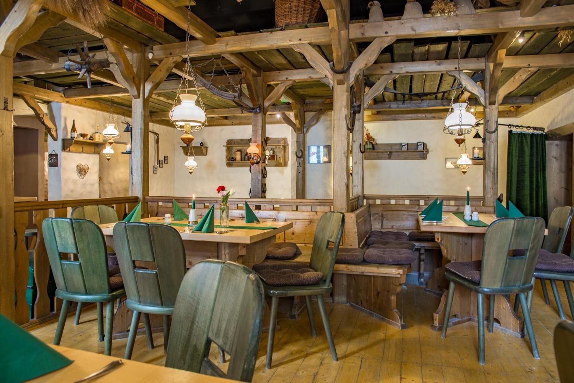 A rustic dining area with wooden beams, green upholstered chairs, and a wooden table.