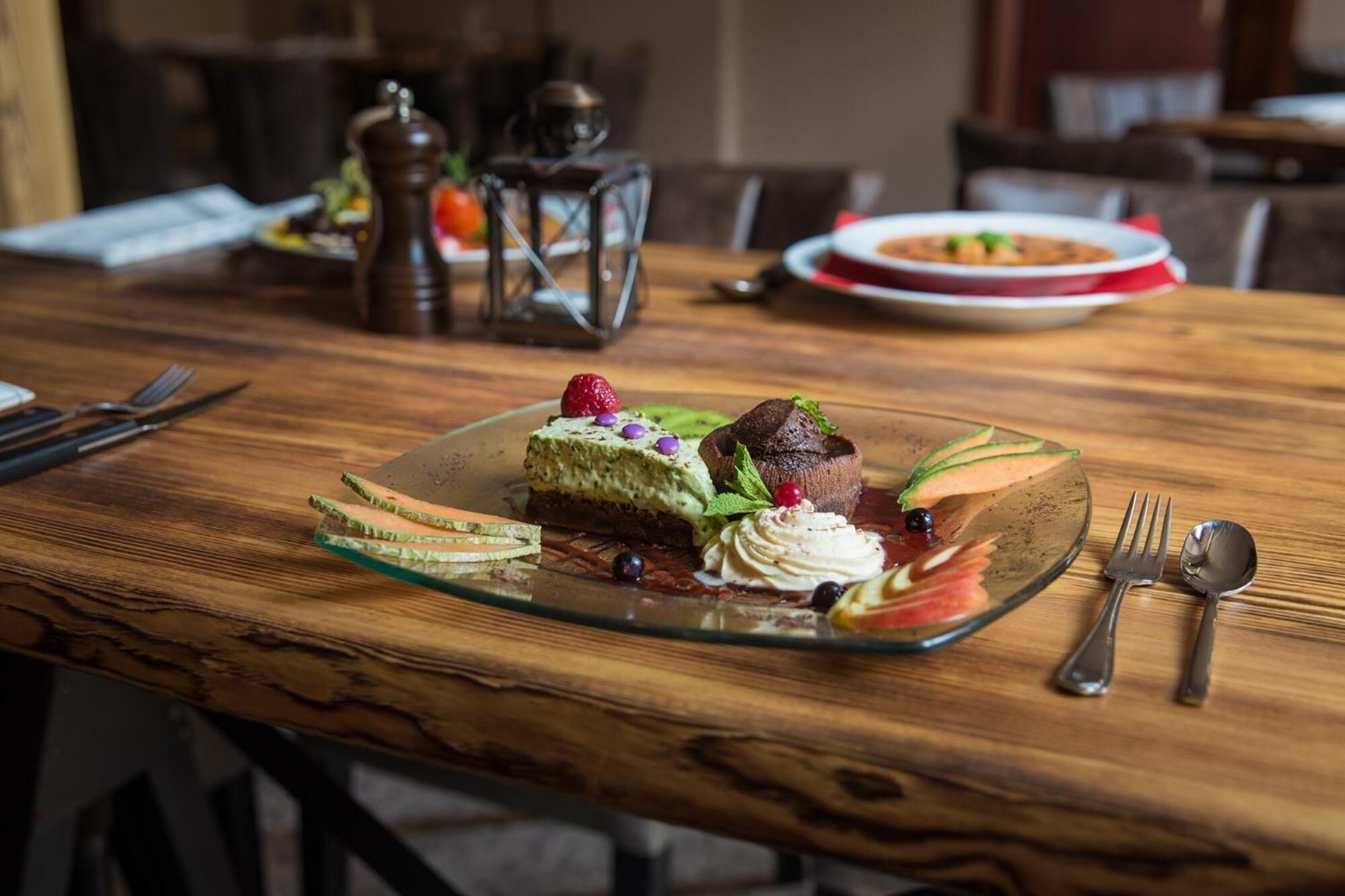 A dessert plate with a layered cake and a chocolate dome on a wooden table.