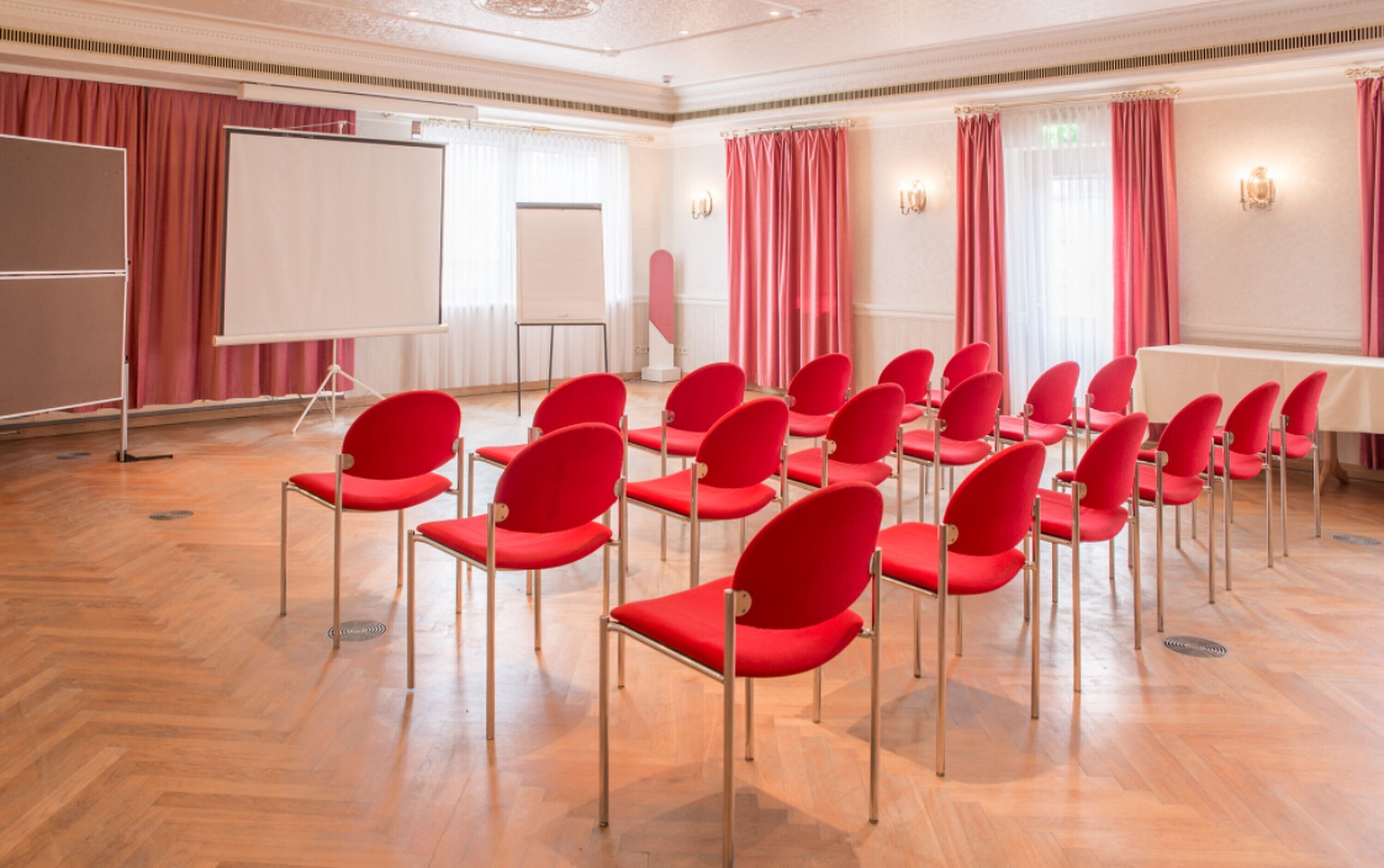 A conference room with rows of red chairs, a whiteboard, and a projection screen.