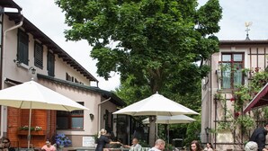 Un café en plein air, avec des tables et des chaises, entouré d’immeubles et d’arbres.