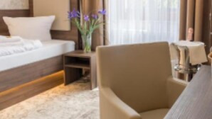 Une chambre d’hôtel avec un lit, une chaise, une petite table et un vase de fleurs.