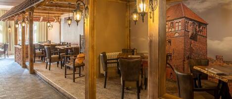 A restaurant with wooden beams, brick walls, and hanging lanterns. Tables and chairs are arranged for dining.