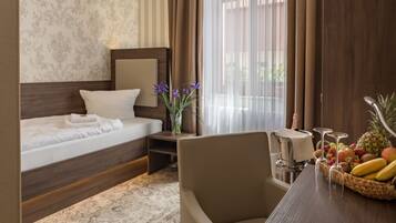 A hotel room with a bed, a chair, a table with fruit and glasses, and a window with curtains.
