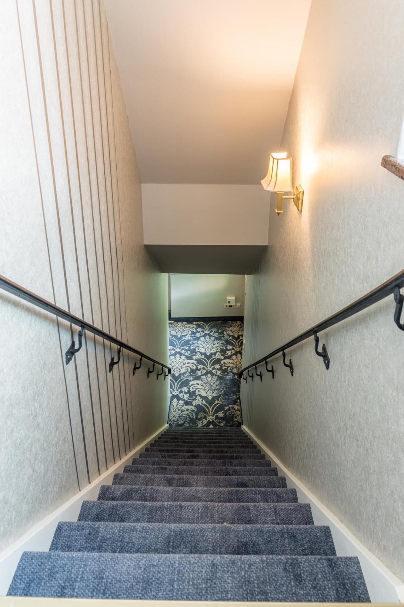 Una escalera con barandilla, peldaños alfombrados y una pared con papel tapiz estampado.
