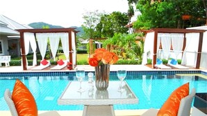 Un área junto a la piscina con dos sillones de mimbre, una mesa de vidrio y un florero con flores.