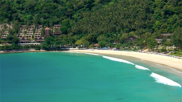 Un complejo turístico costero con una playa de arena y un denso bosque al fondo.