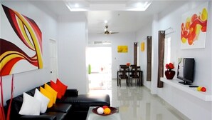 A modern living room with a black leather sofa, a coffee table with fruit, a TV on a white shelf, and abstract wall art. - Green Leaf 2 Nai Harn 2 bedrooms Villa (Rawai)