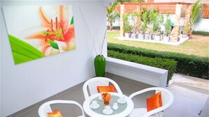 A patio with white wicker furniture, a green vase, and a painting of a flower. - Green Leaf 2 Nai Harn 2 bedrooms Villa (Rawai)