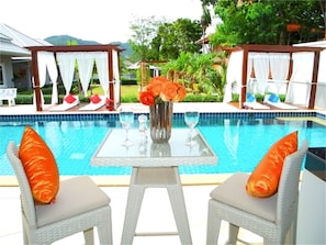 A poolside area with two wicker chairs, a glass table, and a vase of flowers. - Green Leaf Nai Harn 3 bedrooms Villa (Rawai)